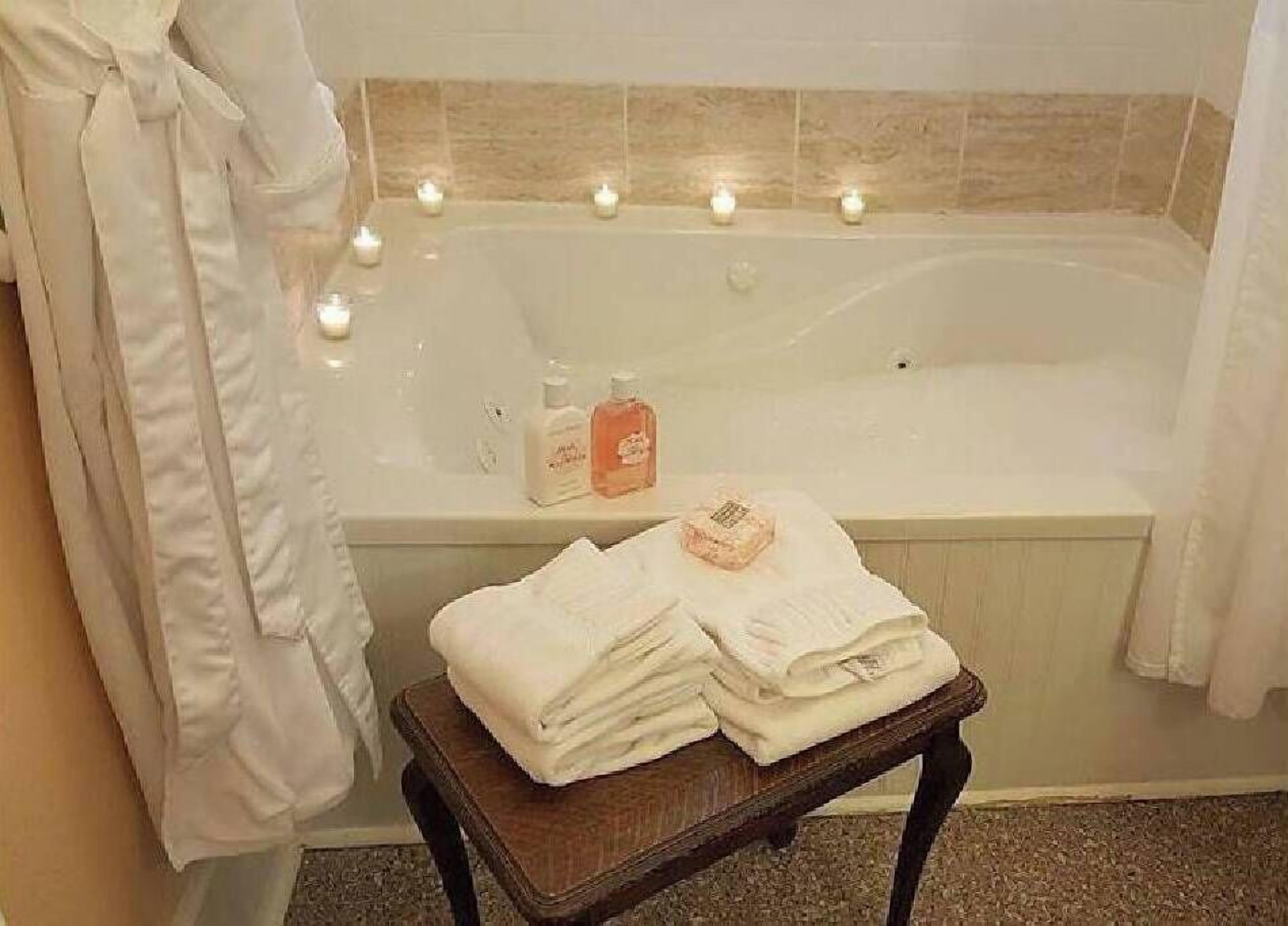 Un baño con bañera, velas y artículos de aseo en una mesita.