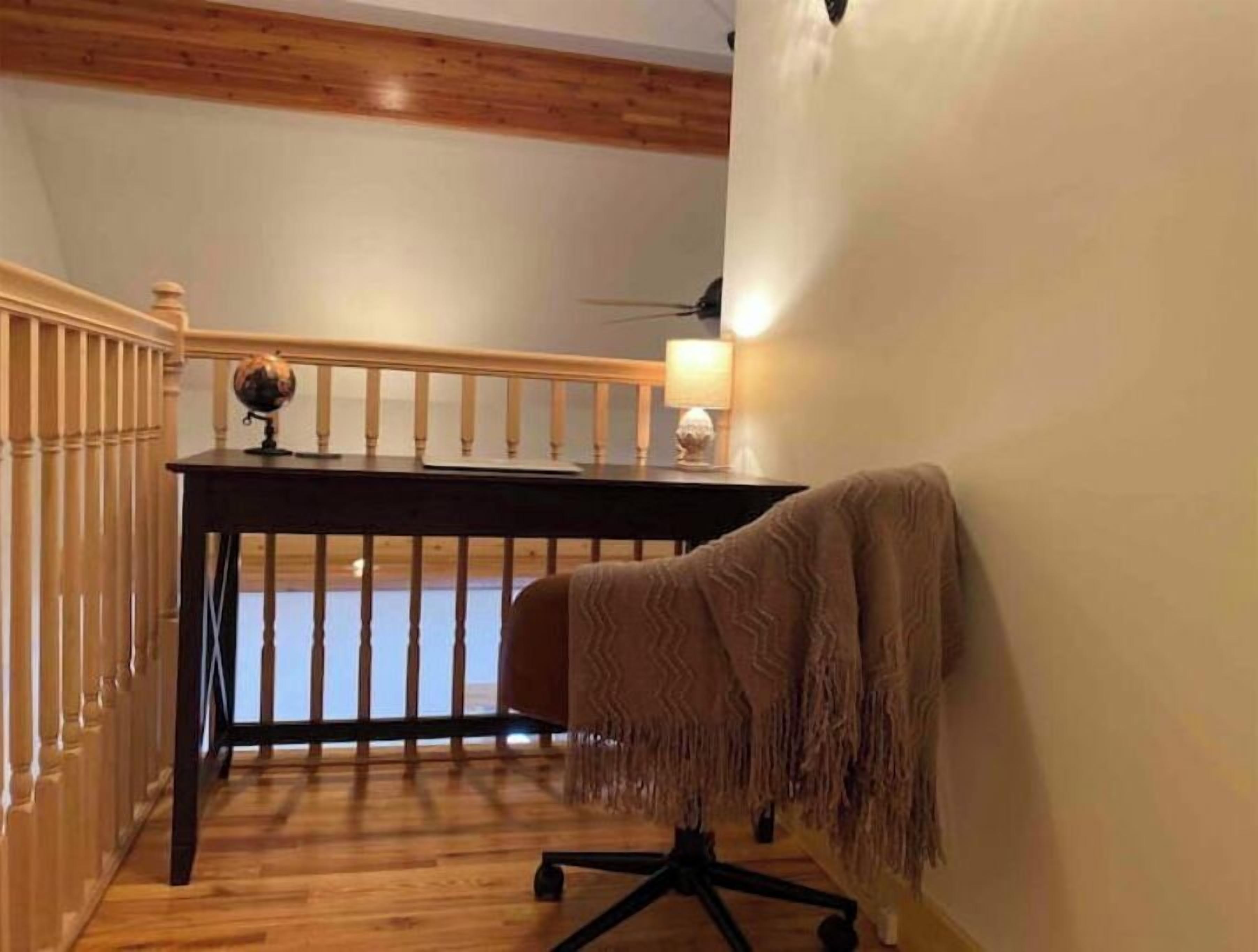 A room with a wooden floor, a desk with a globe, a lamp, and a chair.