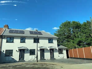A two-story house with solar panels on the roof, a front door, and a fenced yard.