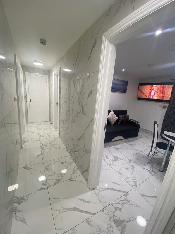 A hallway with marble flooring and walls, leading to a living area with a sofa and a TV.