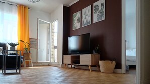 Una sala de estar con piso de madera, un televisor sobre un mueble de madera, un sofá, una mesa de centro y una planta en maceta.