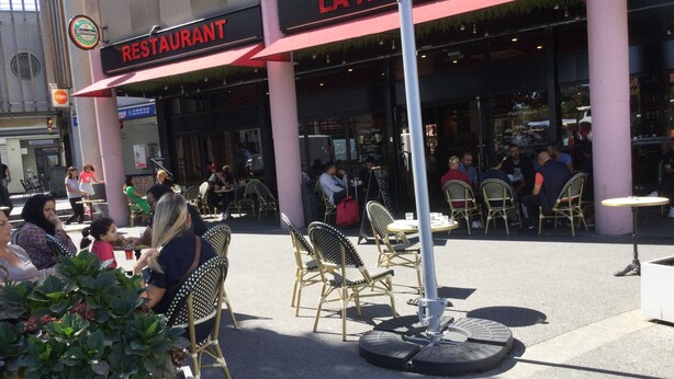 Un área de estar al aire libre con sillas y mesas de mimbre frente a un restaurante llamado "LA ROTONDE".