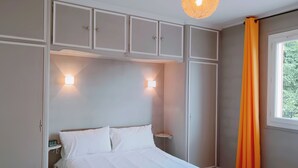 Un dormitorio con cama, armarios empotrados, mesita de noche y ventana con cortinas.