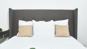 A neatly made bed with a grey upholstered headboard, two white pillows, and a single beige pillow. - Hotel Málaga Managua (Managua)