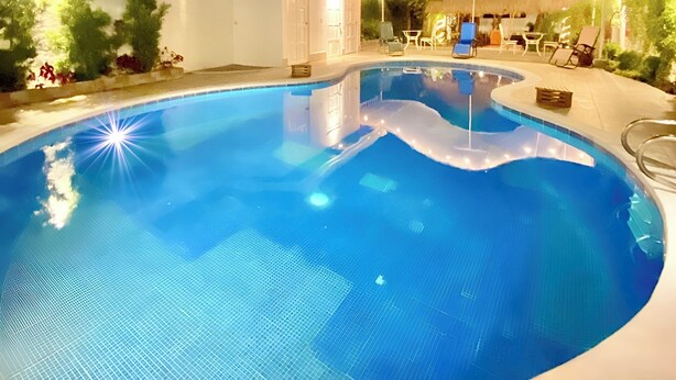 A swimming pool with a curved edge, surrounded by a white wall and a small building. - Hotel Málaga Managua (Managua)
