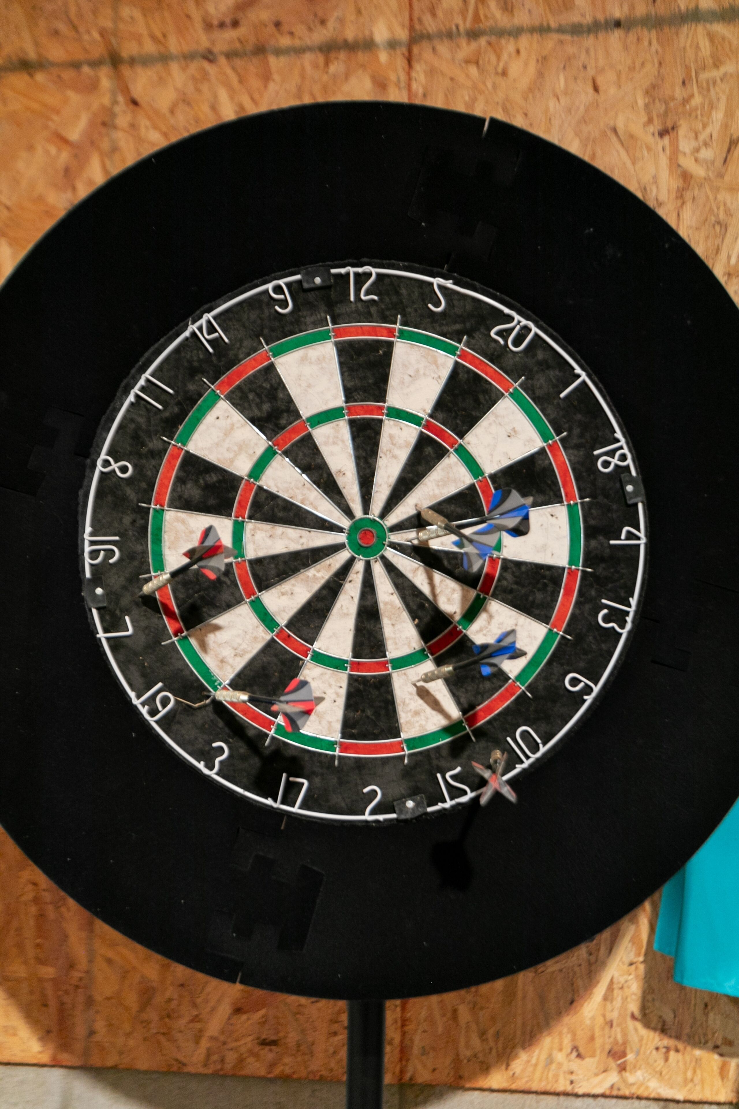 Un tablero de dardos con varias flechas clavadas, sobre un fondo de madera.