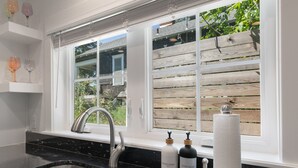 Una cocina con un lavamanos de acero inoxidable, contraventanas de madera y dos botellas de jabón en el alféizar.