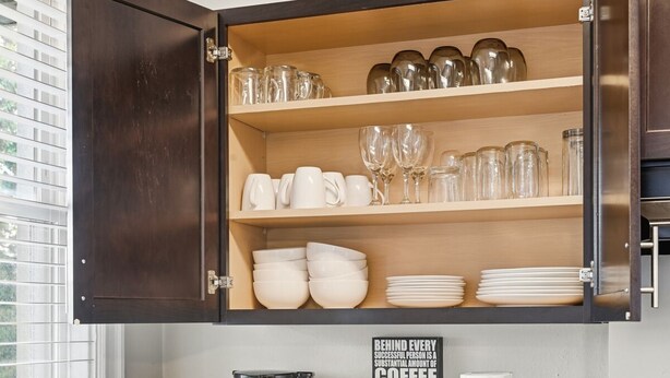 A kitchen cabinet with shelves containing glassware, bowls, and plates.