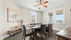A dining room with a wooden table, chairs, a ceiling fan, and a painting on the wall.