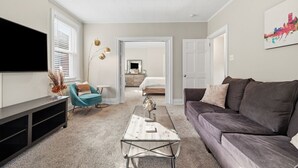 A living room with a sofa, a coffee table, a TV, and a door leading to another room.