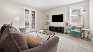 A living room with a sofa, coffee table, TV, and a window with blinds.