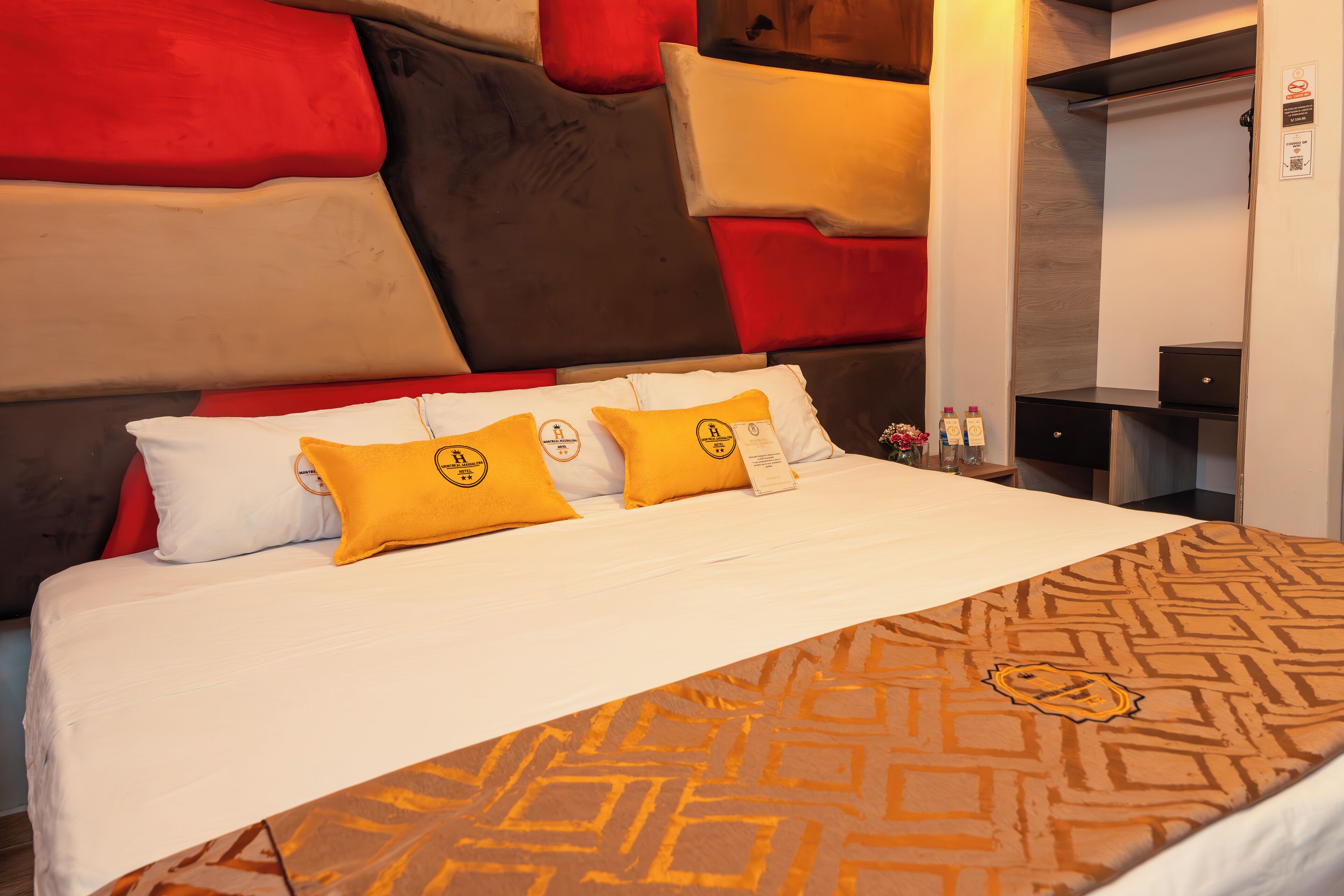 Une chambre d’hôtel avec un grand lit, plusieurs oreillers, une couvre-lit à motifs et une tête de lit moderne.