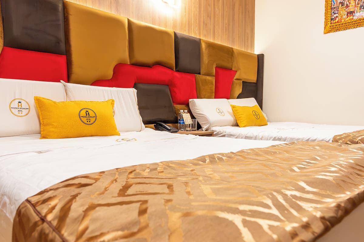 A hotel room with a wooden headboard, a bed with a patterned bedspread, and a nightstand with a phone and glasses.