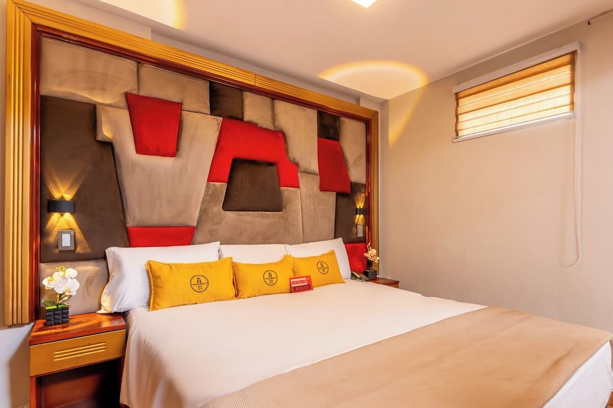 A hotel room with a large bed, a headboard with red and beige panels, and two bedside tables with lamps.