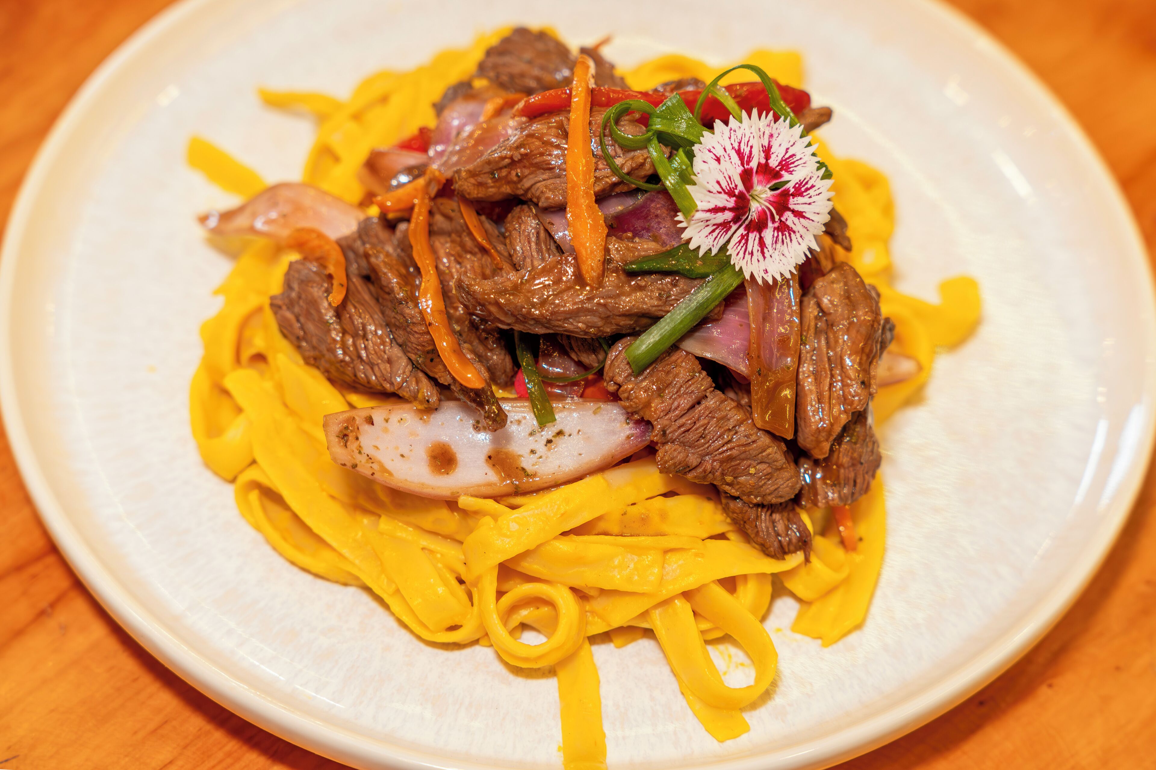 A plate of beef with vegetables and a decorative flower.