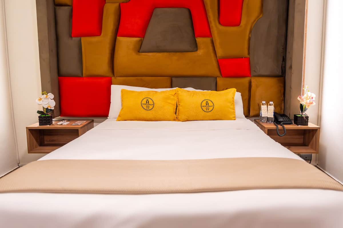 A hotel room with a large bed, two nightstands, a modern headboard, and decorative pillows.