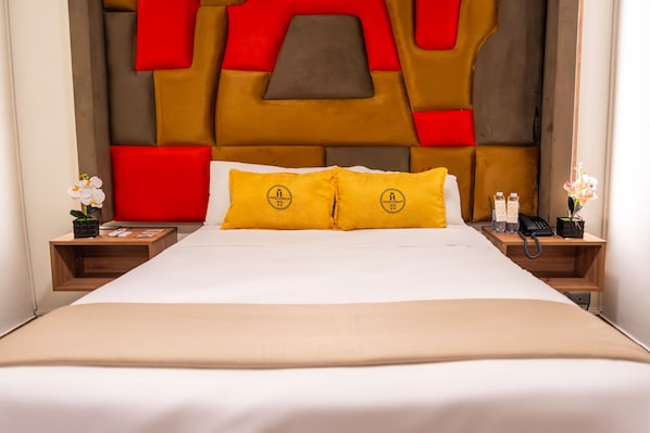 Quarto de hotel com uma cama grande, duas mesas de cabeceira, uma cabeceira moderna e almofadas decorativas.