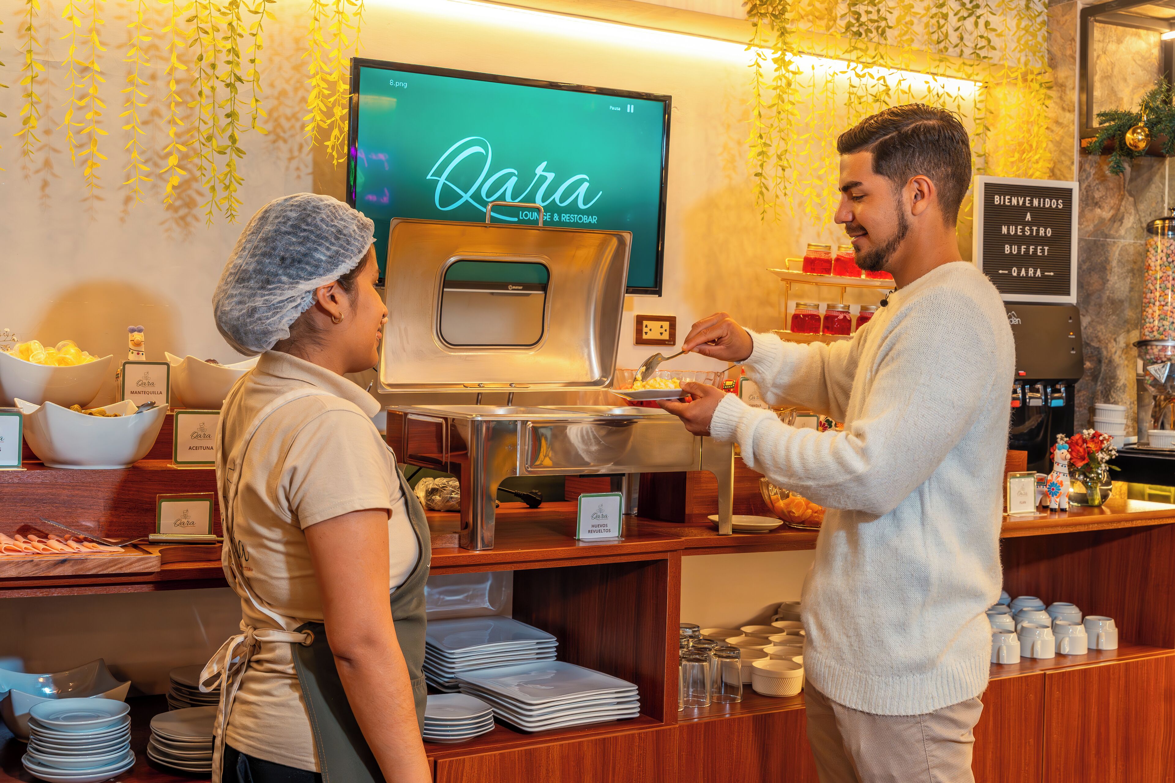 A buffet area with a sign reading "Qara Lounge & Restobar" and a digital screen displaying the same name.