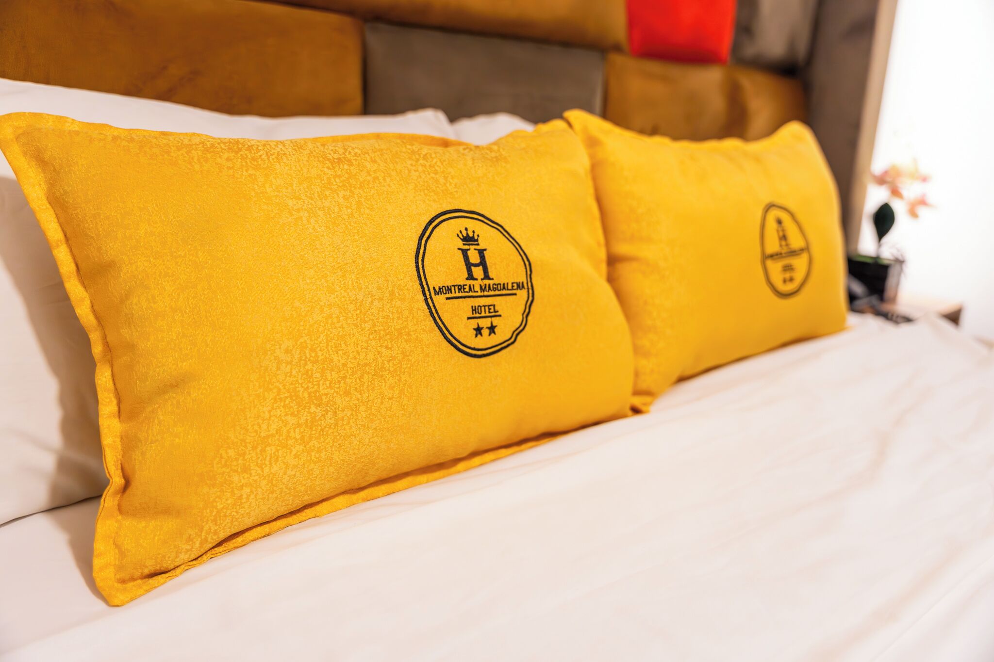 A bed with white bedding and two pillows with a logo and text.