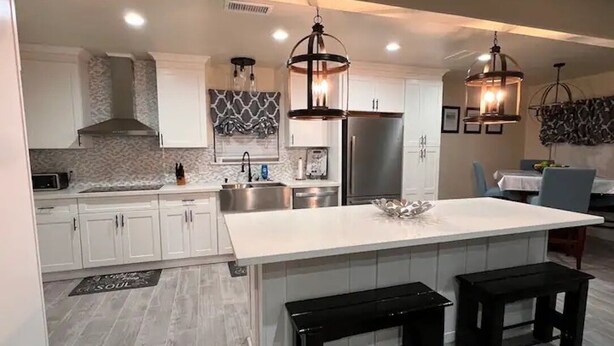 A modern kitchen with white cabinets, a large island, black stools, and pendant lighting.
