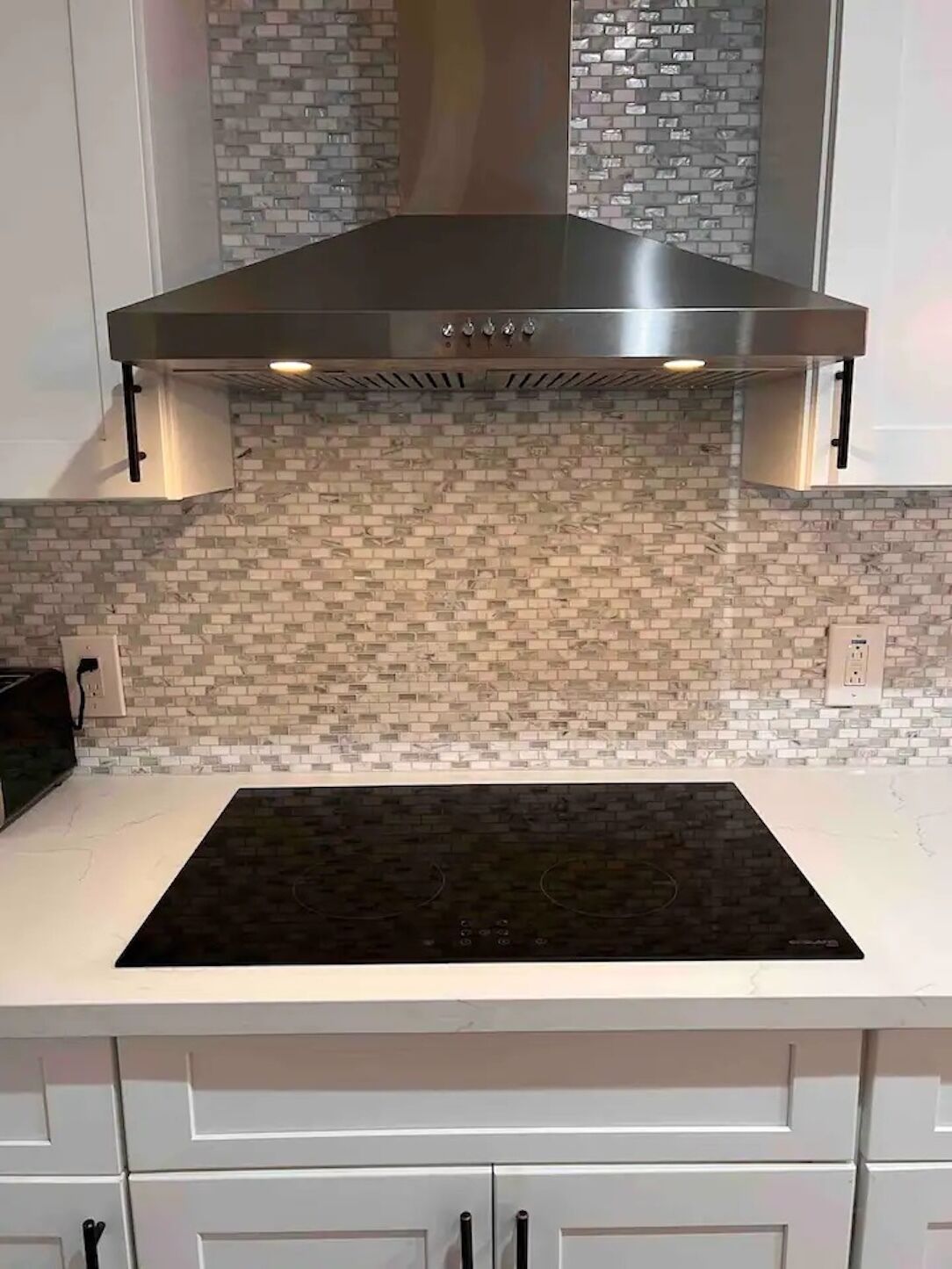 A kitchen with a black induction cooktop, white cabinets, and a backsplash with a mosaic tile pattern.