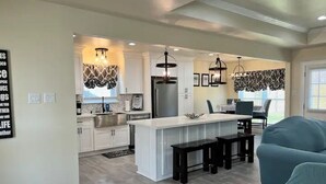A modern kitchen with white cabinets, a central island with black stools, and pendant lighting.