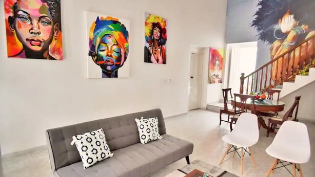 Ein Wohnzimmer mit grauem Sofa, weißen Sesseln und einer Treppe, die in einen Essbereich führt.