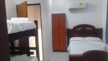 A small, single-room hotel room with a bunk bed, a wardrobe, and an air conditioning unit.
