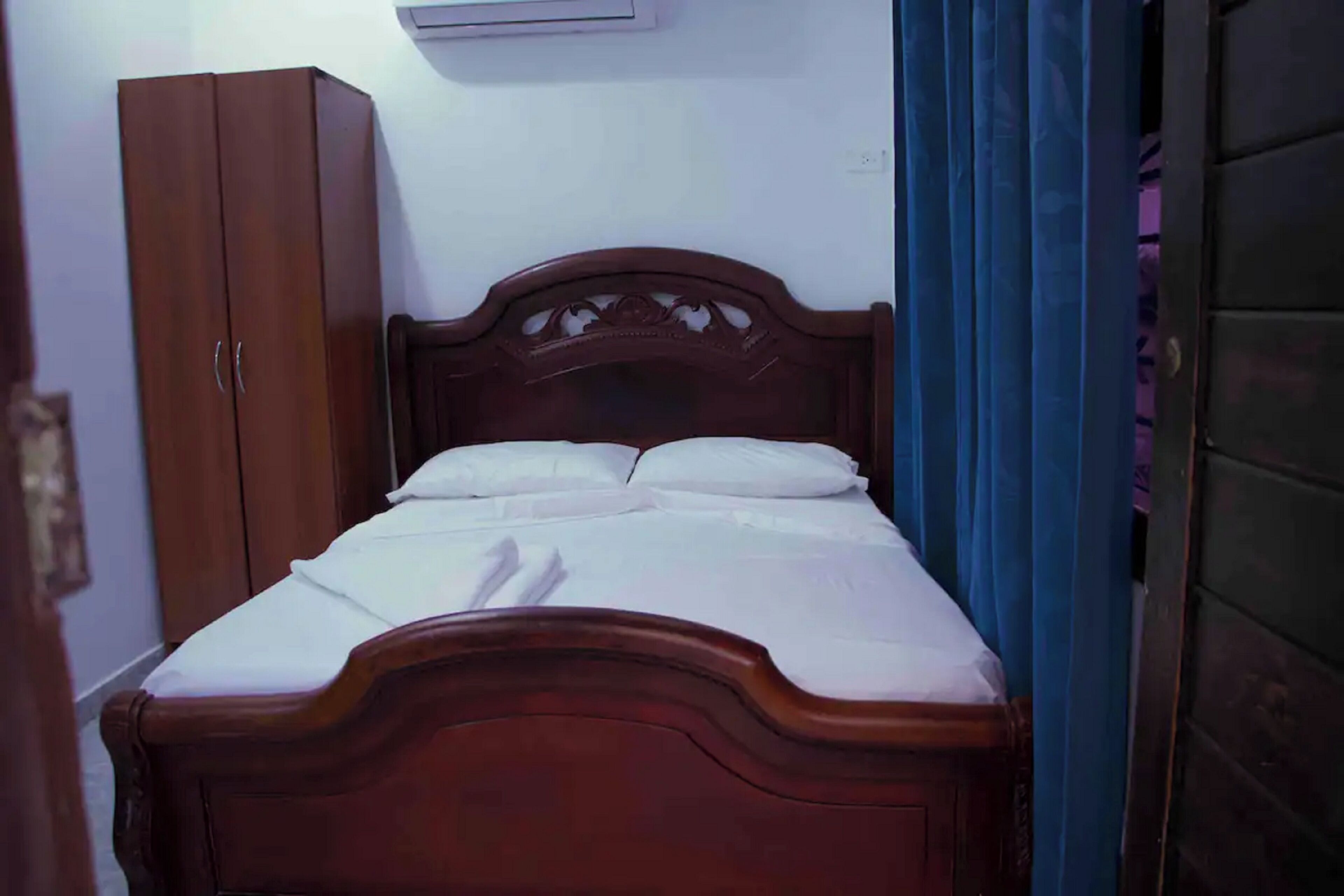 A wooden bed with white bedding, a wardrobe, and a curtain.