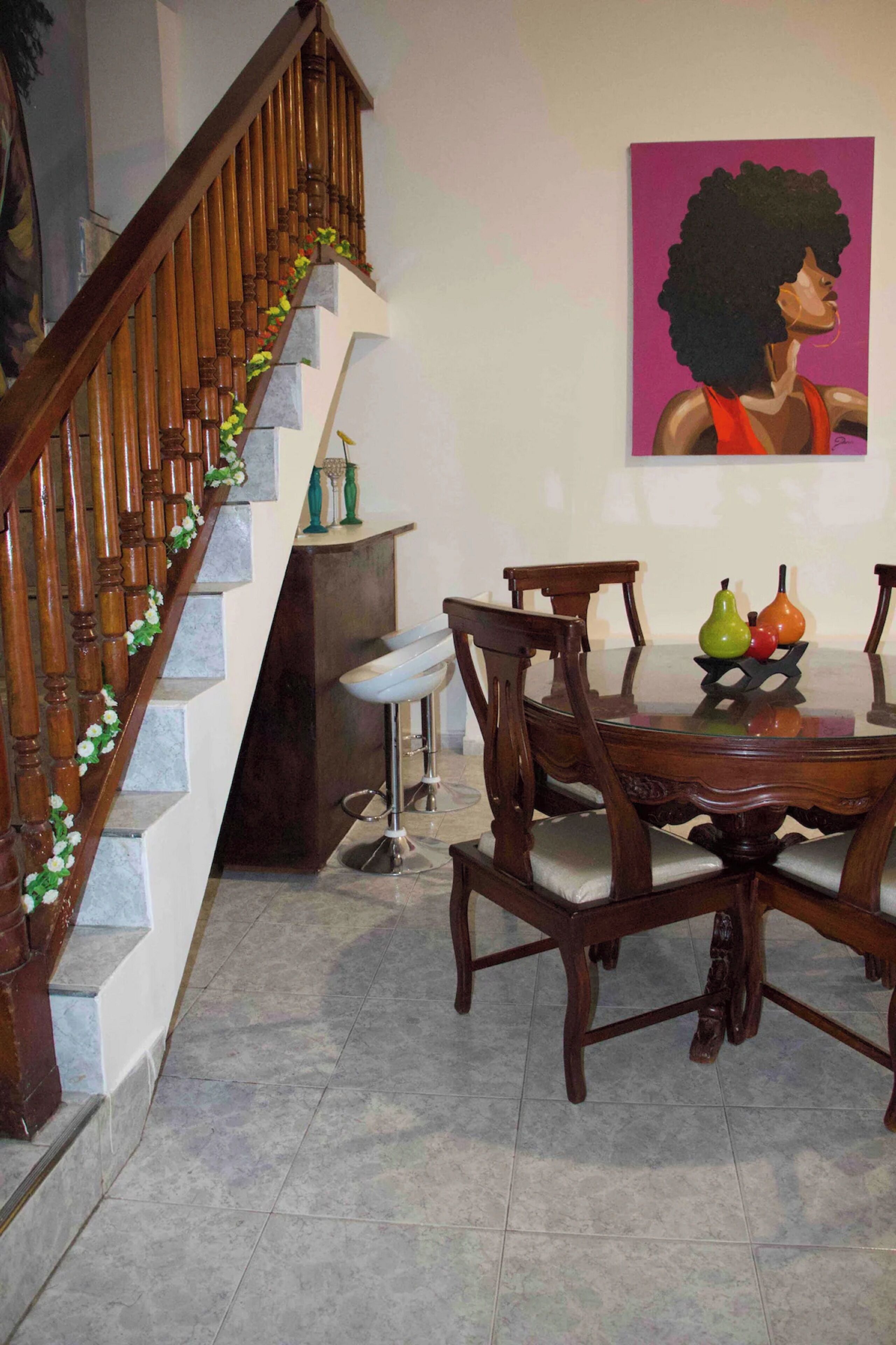 Una escalera con balaustres de madera y baranda de vidrio, una mesa de comedor con sillas y un cuadro en la pared.