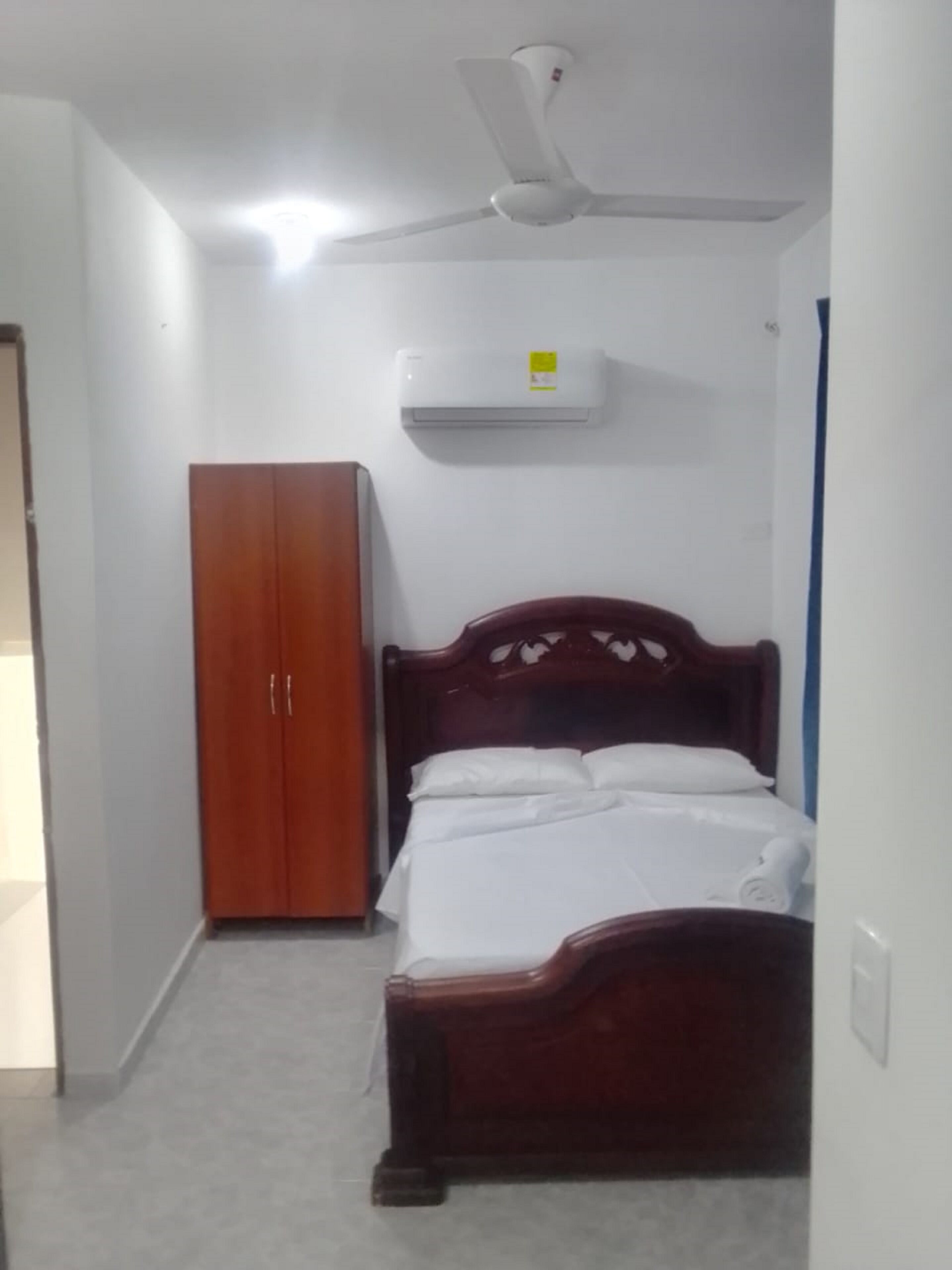 A bedroom with a bed, a wardrobe, a ceiling fan, and an air conditioning unit.