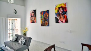 Ein Wohnzimmer mit einem grauen Sofa, einem Holzstuhl und drei farbenfrohen Bildern an der Wand.