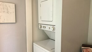 A laundry room with a washing machine and dryer, a white door, and a wall-mounted towel rack. - Puolani Iki-Sweet lil cottage near National Park (Volcano)