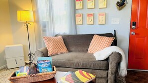 A living room with a sofa, a coffee table with books, a lamp, and framed certificates on the wall. - Puolani Iki-Sweet lil cottage near National Park (Volcano)