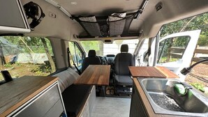 Een gezellig keukentje met een houten tafel en bankje, een gootsteen en een raam met uitzicht op de omgeving.
