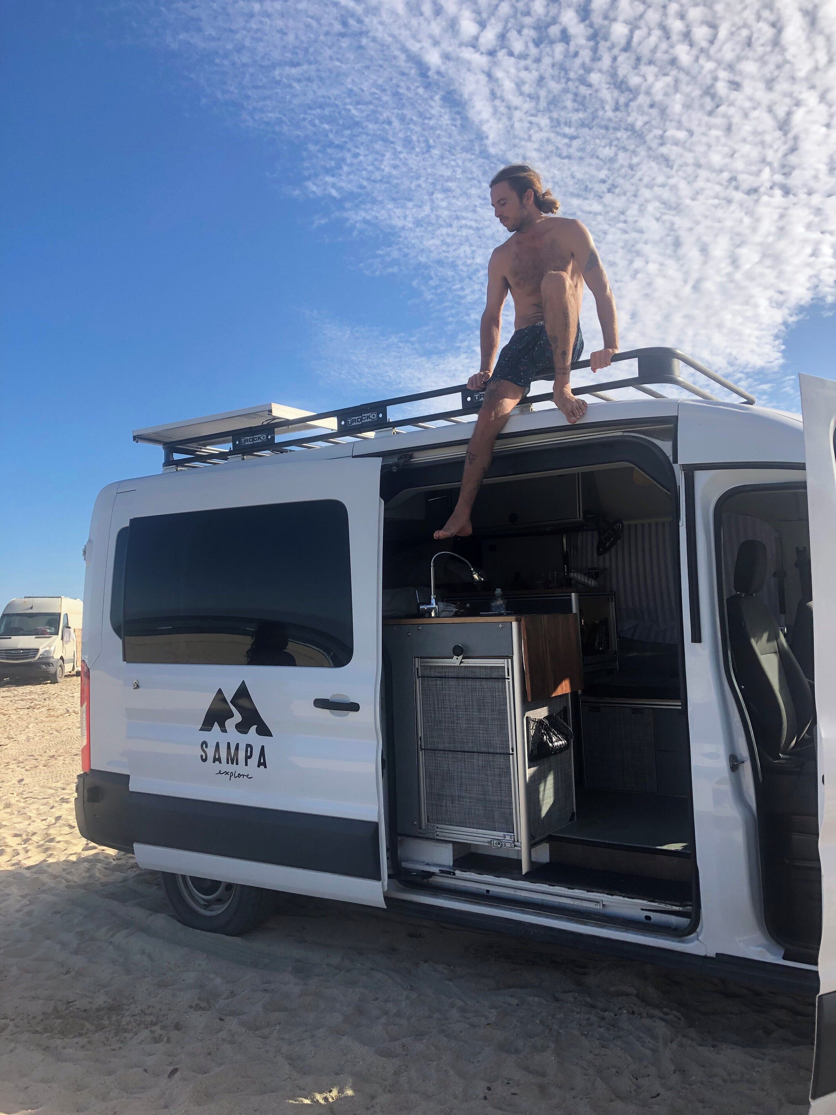 Una camioneta blanca con el logotipo "Sampa Explore" estacionada en una playa arenosa.