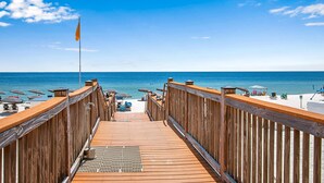 A wooden deck leading to a beach with umbrellas and lounge chairs. - Palacio 805 | Beachfront | Beachside & Indoor Pool, Hot Tub | My Beach Getaways (Pensacola)
