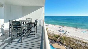 A balcony with a table and chairs, overlooking a beach with clear blue water and a sandy shore. - Palacio 805 | Beachfront | Beachside & Indoor Pool, Hot Tub | My Beach Getaways (Pensacola)