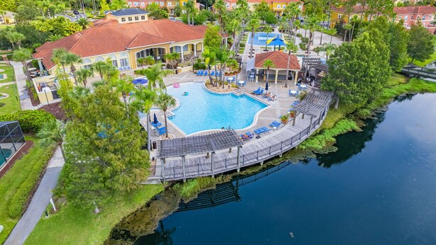 An aerial view of a resort with a central swimming pool, connected by a bridge to a dock.
