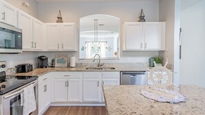 A modern kitchen with white cabinets, a granite countertop, stainless steel appliances, and a decorative wheel.