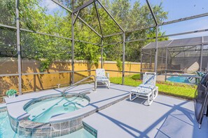 A covered outdoor swimming pool area with lounge chairs and a hot tub.