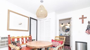 Um quarto com uma mesa redonda de madeira, cadeiras de vime, um candeeiro pendente e um radiador.