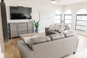 Relax in this stylish living room with a flat-screen TV, comfortable sofa, and ample natural light.