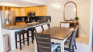 Una cocina moderna con armarios de madera, electrodomésticos de acero inoxidable, una isla central con taburetes y una mesa de comedor con sillas.