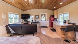 Interior acogedor de una cabaña con techo de madera, un sofá, televisor, zona de cocina y barra.