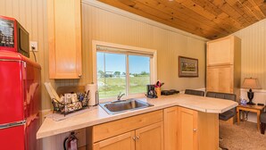 Una cocina con armarios de madera, un refrigerador rojo, un lavamanos y una ventana con vistas al exterior.
