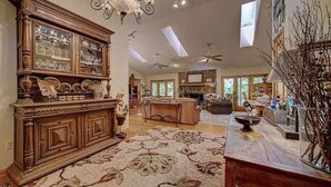 A spacious living room with a large wooden cabinet, a fireplace, and a high ceiling with skylights.