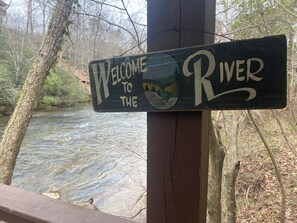 A wooden sign with the text "Welcome to the River" against a backdrop of a flowing river and trees.