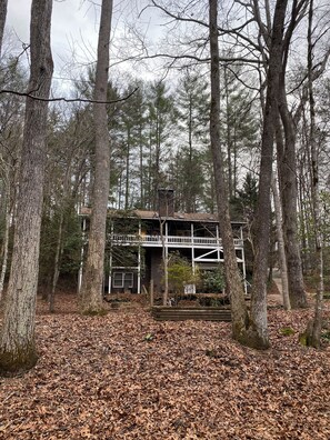 Ein zweistöckiges Holzhaus, umgeben von hohen Bäumen und einem mit Blättern bedeckten Boden.
