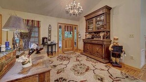 A spacious living room with a large wooden cabinet, a chandelier, and a floral carpet.